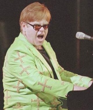 Sir Elton John playing the piano in green
